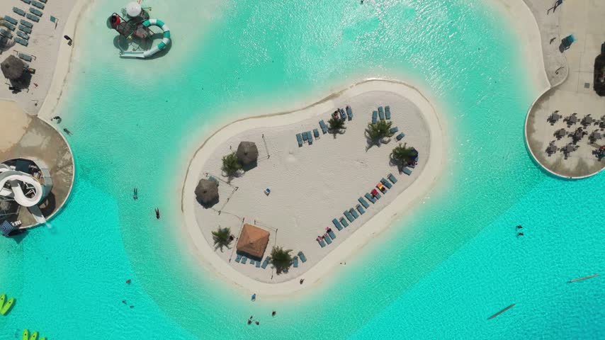 Overhead drone view of a private-feeling sandy island oasis in the middle of the turquoise lagoon in San Antonio, Florida, with palm trees and lounge chairs.