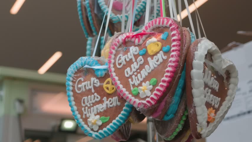 Several heart shaped gingerbread cookies hang side by side on colorful ribbons, each decorated with glossy sugar icing and the handwritten message Greetings from Munich.