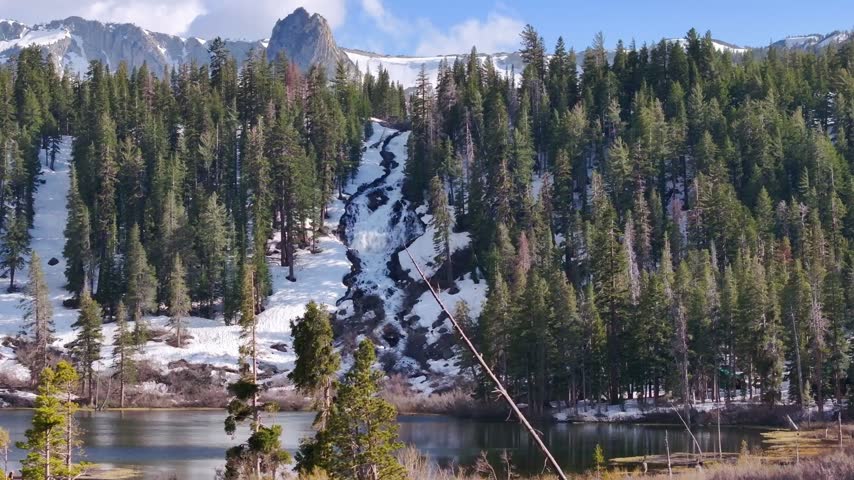 Cinematic aerial view of Twin Lakes in Mammoth Lakes, California, featuring evergreen forests, rugged alpine terrain, and dramatic mountain peaks surrounding the glacial basin