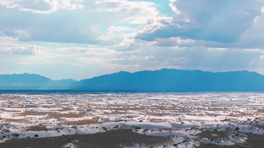 aerial wide angle panorama of glistening gypsum dunes in White Sands National Park, New Mexico, showcasing the expansive arid desert floor, natural textures, and distant mountain range.