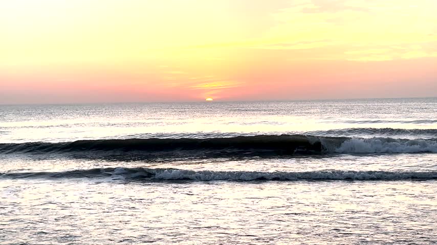 The sun rising over the ocean in Corolla North Carolina with Ocean waves crashing gently on the shore.