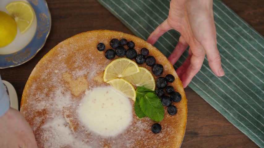 Hand presenting finished lemon blueberry cake in cozy kitchen