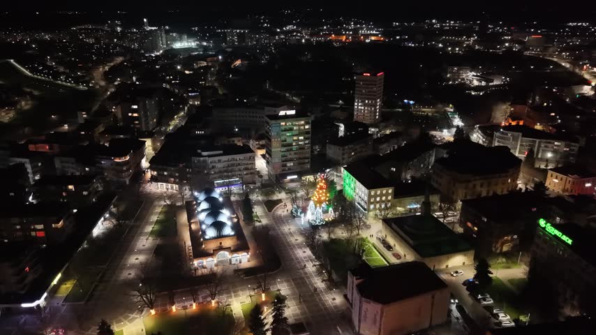 Scenic night drone shot of the historic Ottoman covered market Bezisten in Yambol, Bulgaria. The central town square is beautifully illuminated with festive Christmas lights, holiday decorations, and a glowing Christmas tree.