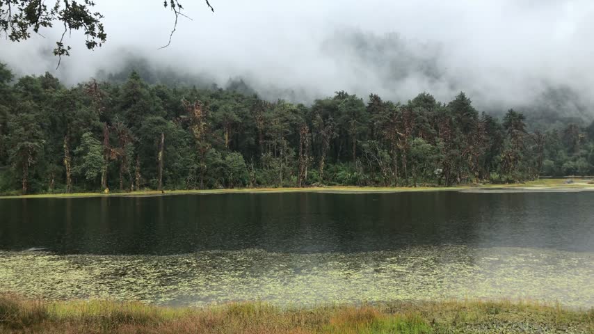 Rain falling over the Ramaroshan Lake, encircled by lush, forested hills, as clouds drift slowly above in far-western Nepal