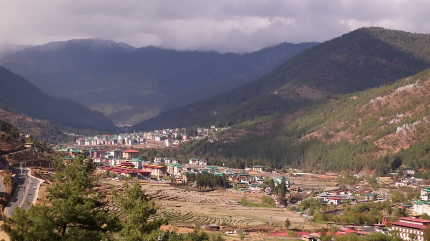 Bhutan Capital City Thimphu Spreads Across Green Valley Beneath Storm Clouds and Forested Peaks