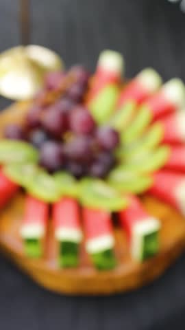 A tropical platter with watermelon, grapes, and chopped kiwi is served on a wooden buffet during a social event. Concept of healthy food and gourmet 