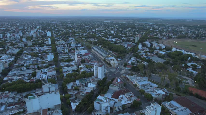 4K drone aerial view of La Plata, Buenos Aires, Argentina at sunset. Urban skyline, buildings and streets illuminated by warm evening light across the city.