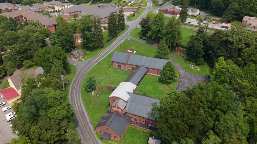 Drone shot panning over the historic stone furnace buildings, parking area, and green surrounding foliage at Cornwall Iron Furnace in Pennsylvania.