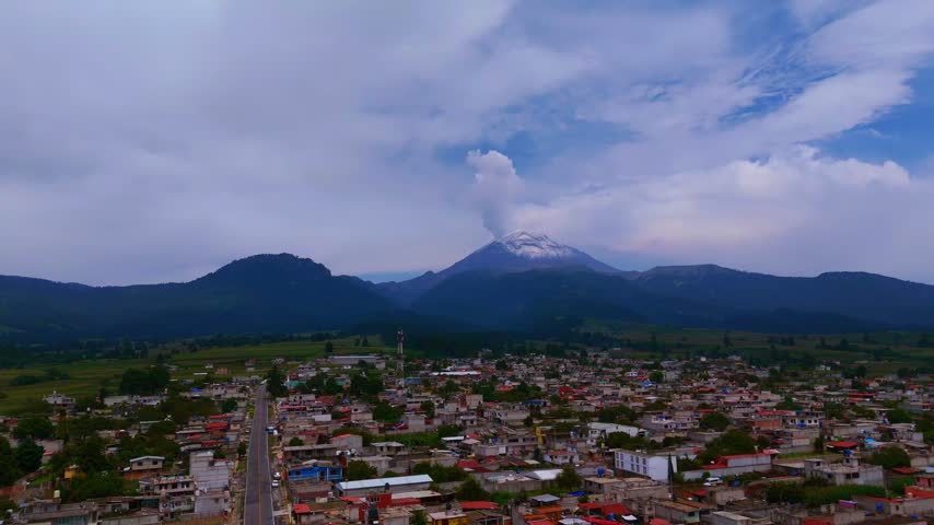 Drone footage capturing a scenic Mexican town with a looming volcano in the distance,Drone footage of town with mountains in distance
