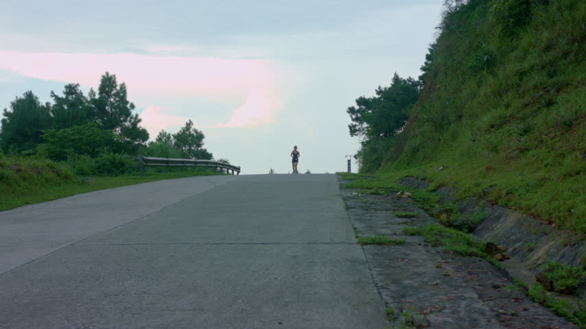 Female runner jogging uphill along a paved mountain road during sunset at Mau Son, Vietnam. Outdoor cardio endurance training and active travel lifestyle