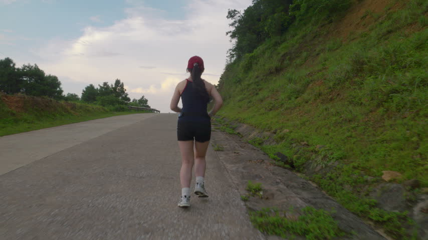 Asian woman jogging away along an empty mountain road during twilight in Mau Son, Vietnam, engaging in outdoor cardio fitness.