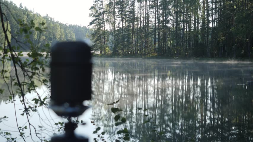 A static view of heat distortion rising from an out-of-focus camping pot in the foreground, with morning fog drifting across a calm forest lake.