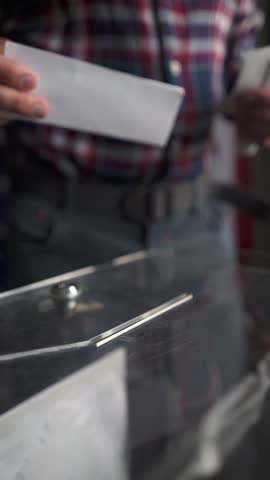 Voter walking up and inserting ballot into slot of transparent box, front view