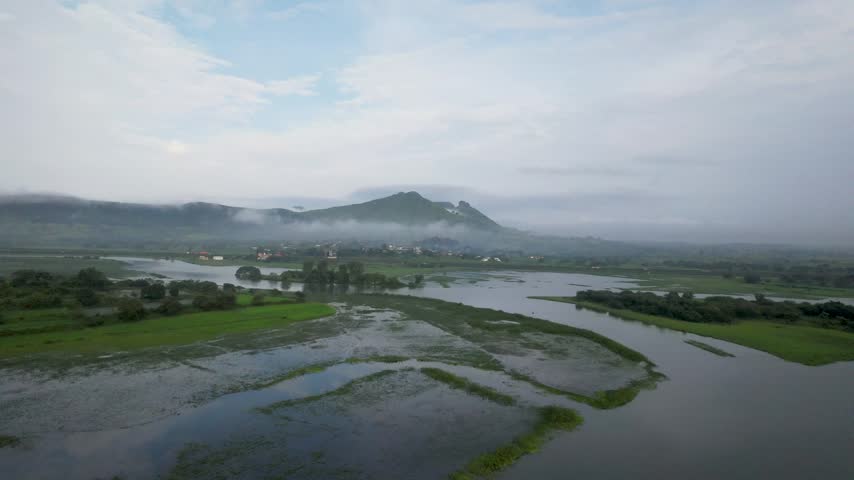 Aerial panorama of wetlands with misty mountains and lush green landscape.