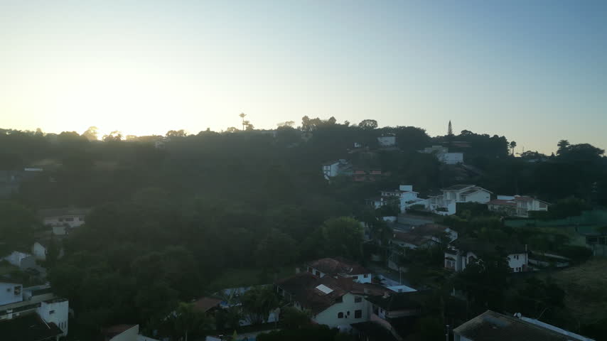 Aerial drone footage revealing a beautiful golden sunrise over Carapicuiba in Sao Paulo state, Brazil, with warm morning light and sun rays spreading across the urban landscape.