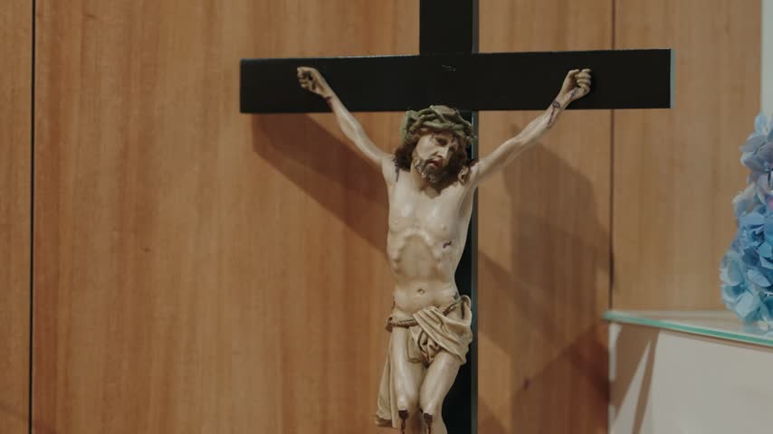Carved Christ figure on a dark cross against a light wood panel wall inside a chapel