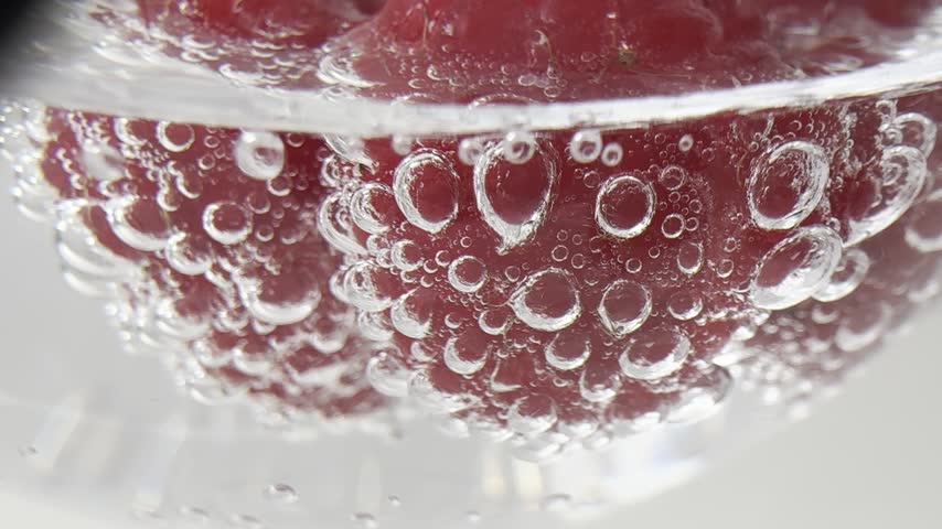 Bubbles surrounding red raspberries in sparkling water. The bubbles move around the raspberries.