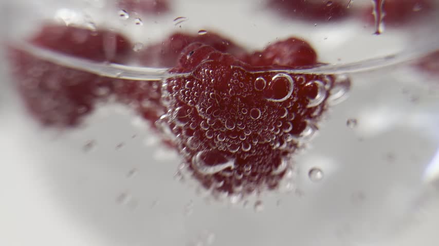 Bubbles surrounding red raspberries in sparkling water. The bubbles move around the raspberries.