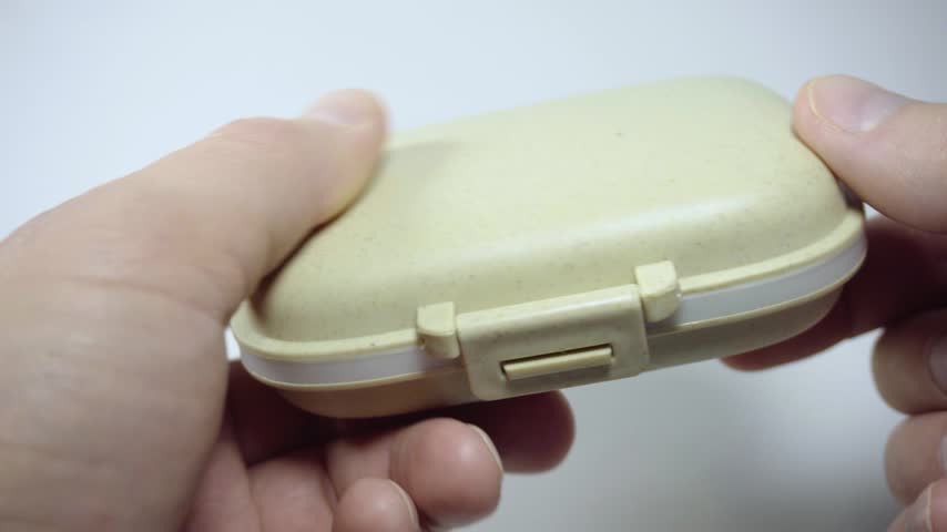 Close up of hands opening a pill organizer and showing tablets inside. Medication storage container for organizing daily medicines and supplements at home