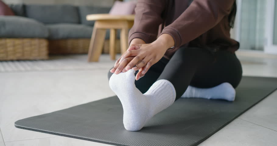 Post warmup African American woman doing seated stretches on black mat at home hoodie white-sock. Yoga, flexibility, stretch, balance, relaxation, livingroom, fitness
