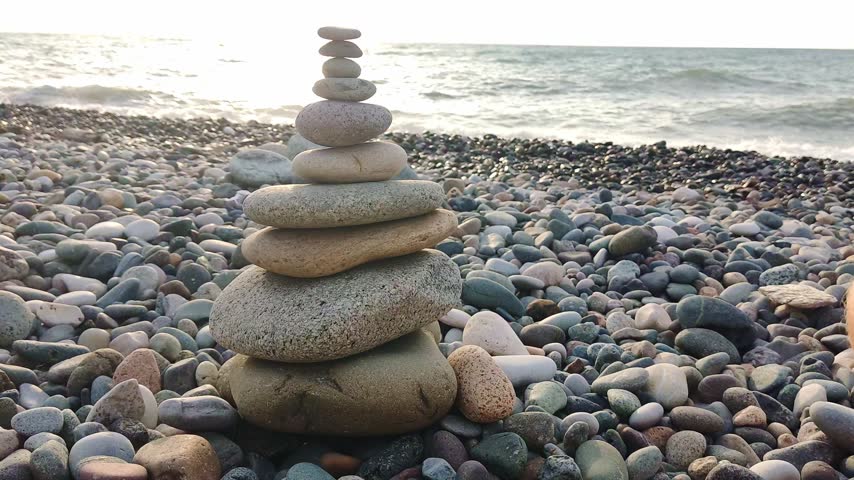 Pyramid of sea pebbles balanced on stone beach, zen stones stack on ocean coast background, balance harmony and mental health wellness concept.