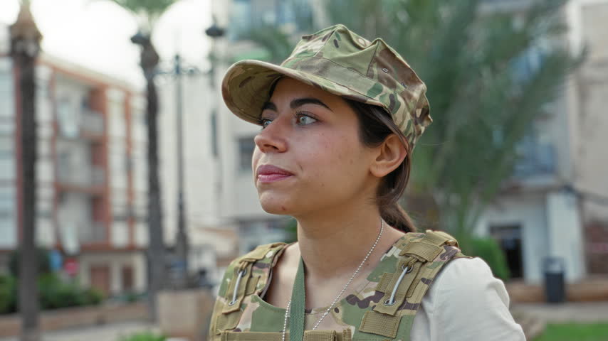Young woman soldier in camouflage blows a kiss with hand to lips on a residential street; affection duty.