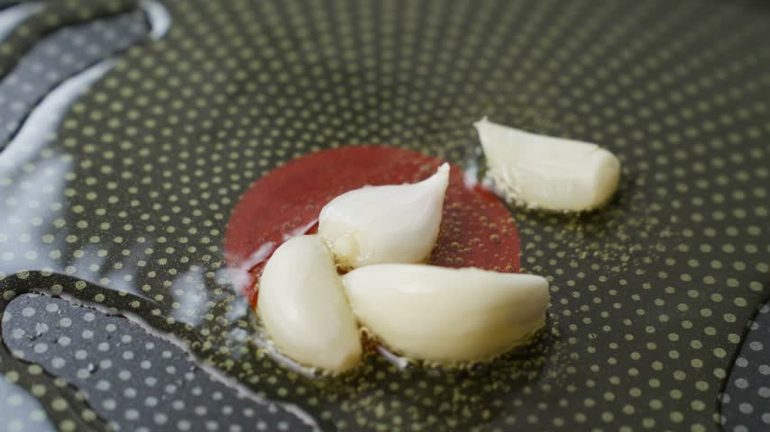 Red spatula stirs garlic cloves in hot oil on a frying pan. Concept of home cooking and food preparation