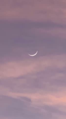 A beautiful timelapse of a crescent moon appearing among orange clouds during twilight.