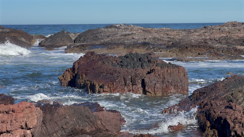 Rocky coastal shoreline at Punta Ballena, Uruguay, with a large rock formation in the ocean and waves rolling into the smaller rocks