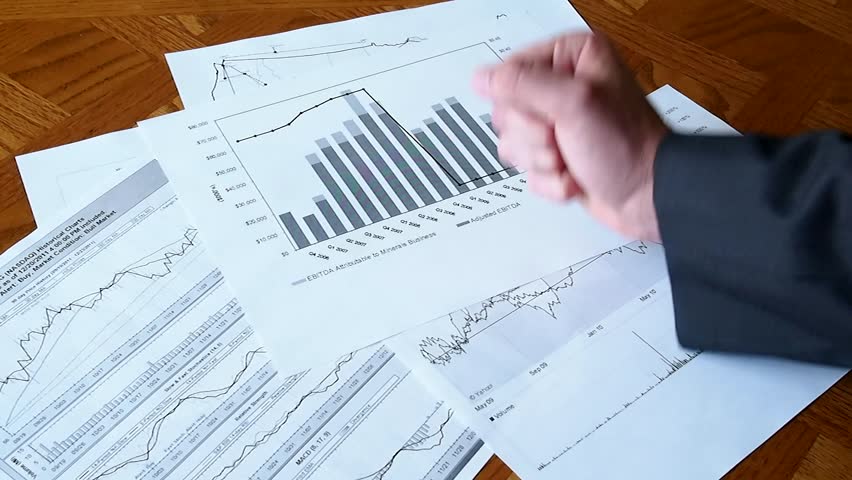A business man looks at a graph on the table and bangs his fist on the table.