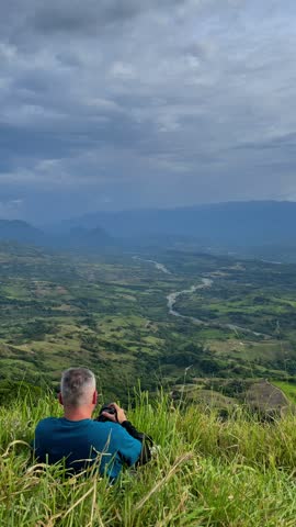 Travel Photographer Taking Pictures of Scenic Mountain Valley Landscape with River Under Dramatic Cloudy Sky