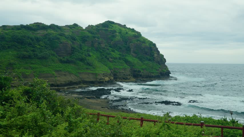 Green cliffs overlook black sand beach and waves at Yongmeori Coast Jeju