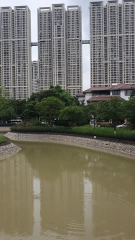 Urban pond surrounded by green trees and modern residential buildings in Hanoi, Vietnam.
