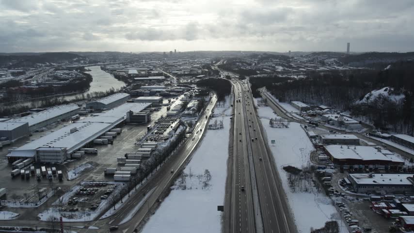 Aerial drone view of E6 highway, industrial area, logistics center, and river landscape in Bäckebol, Hisingen, Gothenburg, Sweden, covered in snow during winter.