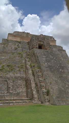 Vertical static low angle shot of the ancient Pyramid of the Magician structure at Uxmal archaeological site in Yucatan, Mexico under blue sky.