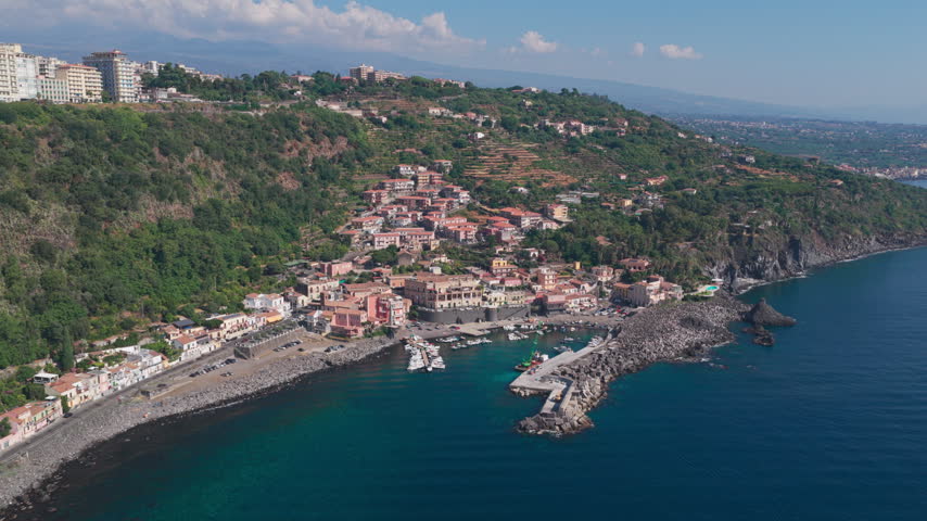 Establishing aerial of Santa Maria la Scala, a fishing village surrounded by basalt black lava cliffs near Mount Etna in Acireale, Catania, Sicily, Italy, a popular destination on the Ionian coast.
