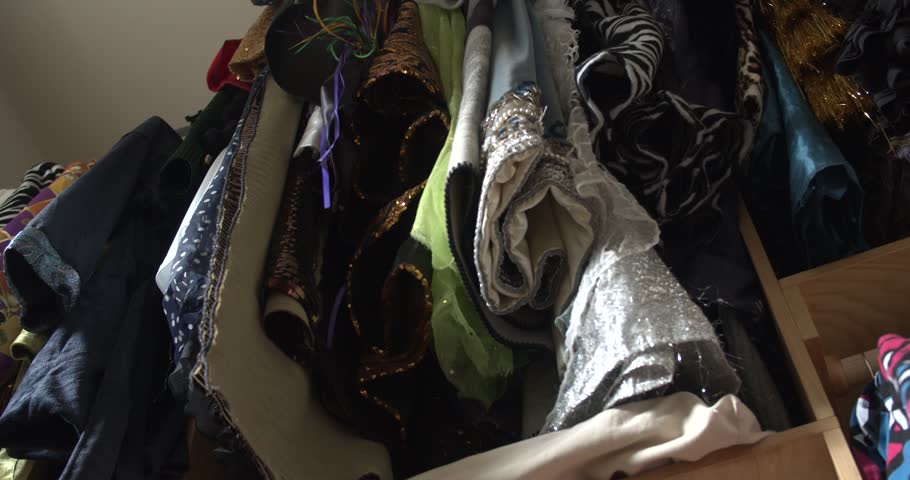 A slow pullback from beneath a rack of colorful Mardi Gras costumes, revealing layers of clothing, fabric, and accessories filling a crowded closet.