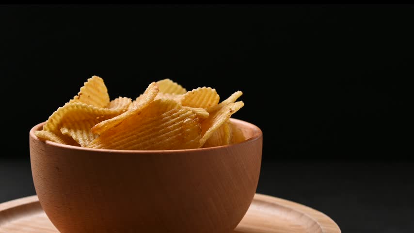 Bowl of potato chips rotating on black background