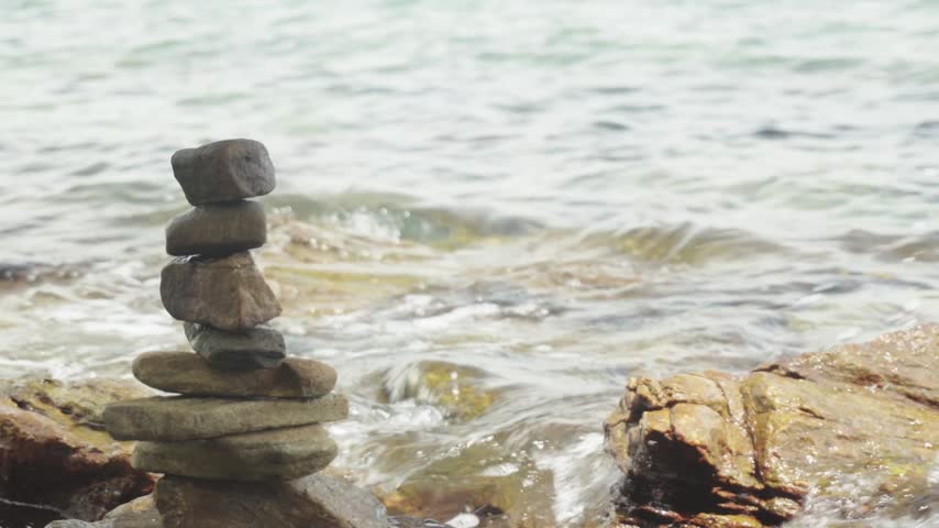 A balanced stack of flat coastal stones evokes a sense of peace, harmony, and meditation against a softly blurred background of rolling ocean waves