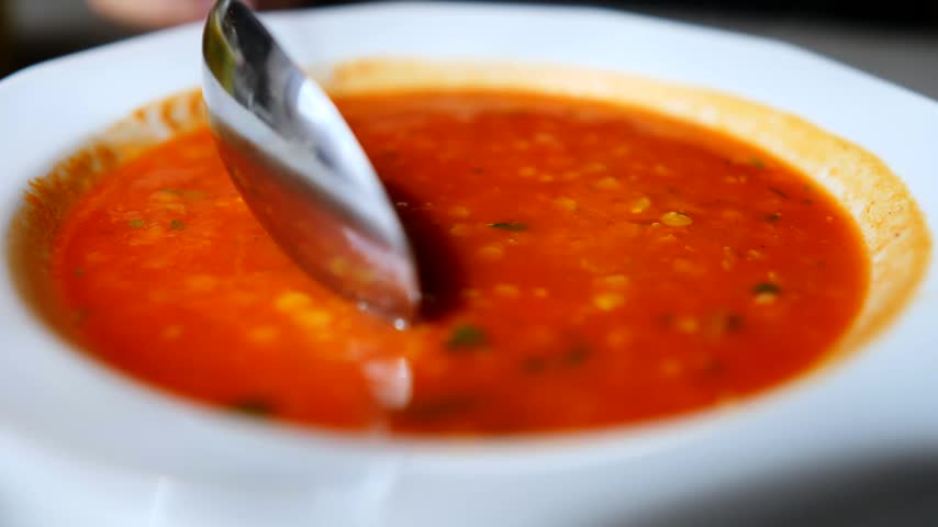 Close up view of a person stirring and eating a hot, steaming bowl of red lentil soup with a spoon. Nutritious and comforting vegetarian dish, perfect for lunch or dinner
