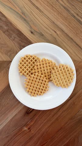 Female Hand Picking Up Pizzelle Cookie From White Plate