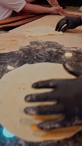 Vertical shot of round lahmacun dough being rolled and prepared at a traditional lahmacun bakery in Turkey.