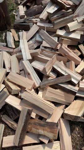 Close-up of freshly split firewood piled outdoors on the ground in natural sunlight. Chopped wooden logs showing bark, wood grain, and rough textures, prepared for heating or an outdoor fire.