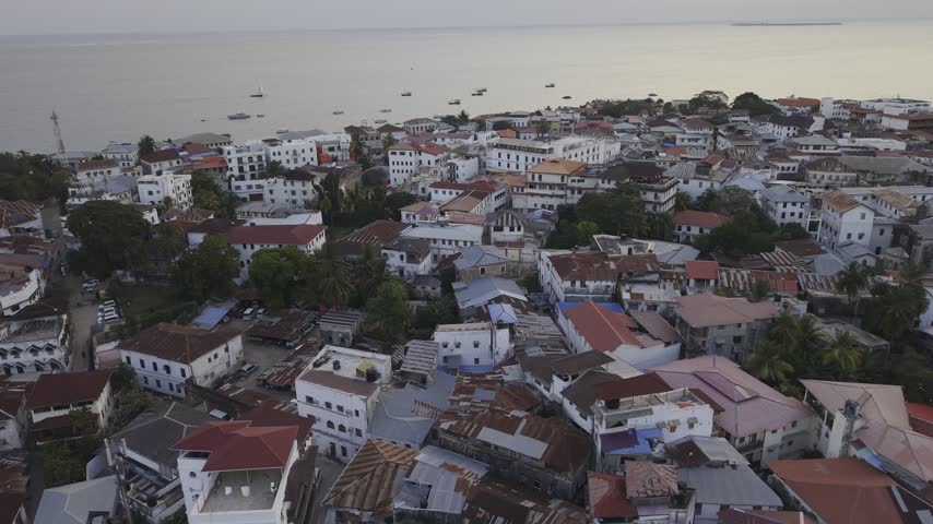 Drone flies low over Stone Town during a cloudy sunset in Zanzibar, Tanzania