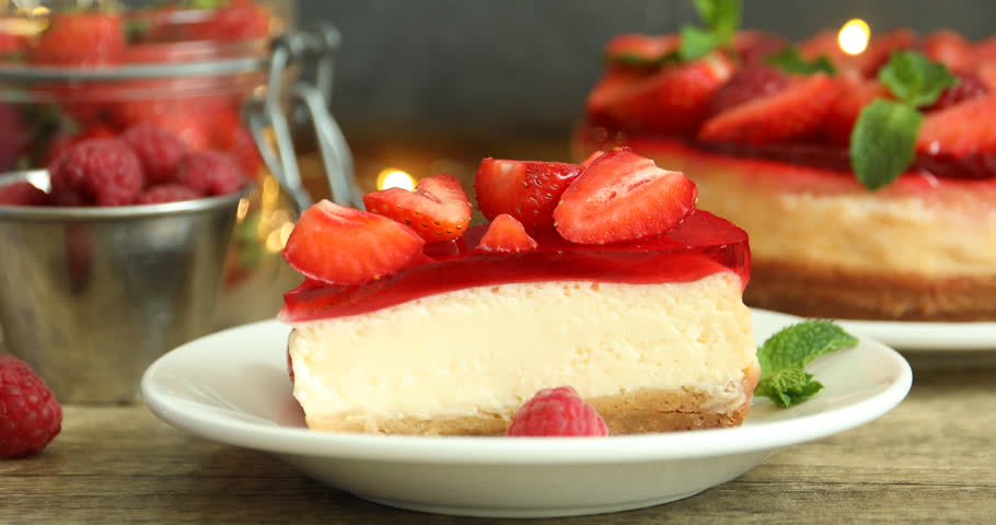 Woman putting mint onto piece of delicious cheesecake with strawberry jelly and fresh berries at wooden table, closeup