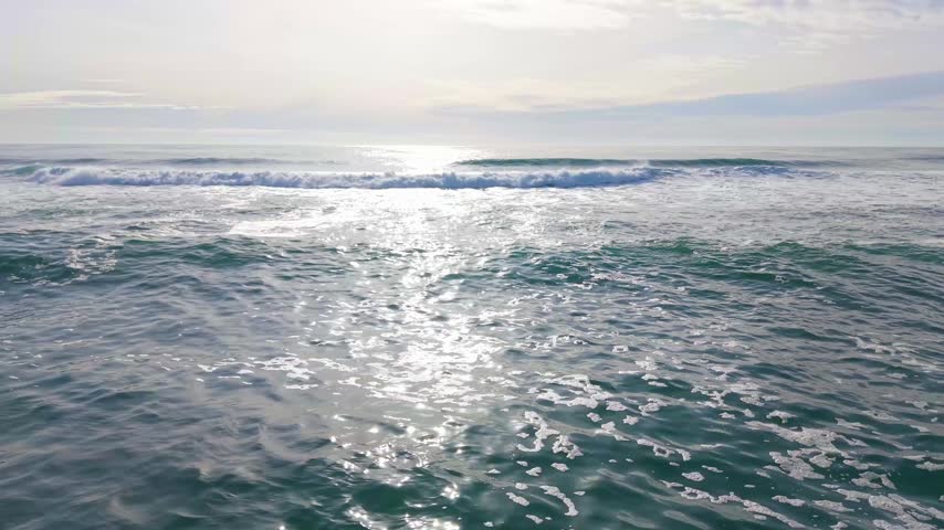 Aerial flight over rolling Pacific Ocean waves along the Oregon Coast near Manzanita, capturing textured surf and shimmering water.
