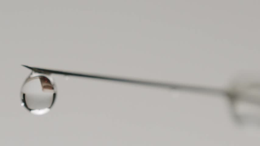 Macro shot of a medical syringe needle dripping a clear liquid drop, representing vaccination, medication, or scientific research, isolated on a clean, sterile white background.