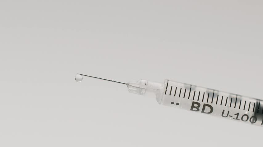 Medical syringe needle slowly dripping clear liquid in a clinical laboratory setting. vaccination, injection, and pharmaceutical research. Macro shot of an insulin syringe with a needle