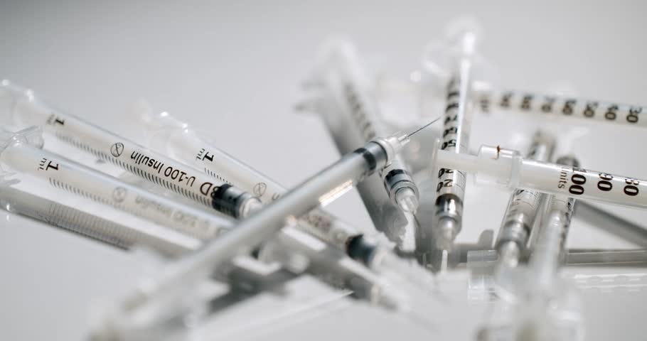 Many insulin syringes rotating on a white reflective surface, representing concepts like diabetes management, medical treatment, vaccination, or healthcare and pharmaceutical industries.
