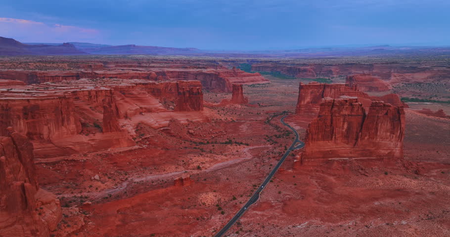 Vast deserted landscape of the National Arches Park in Utah, USA with spectacular red rocks. Few cars ride by the highway crossing the scenery. Aerial view.